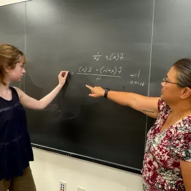 Two people at a chalkboard solving a math problem